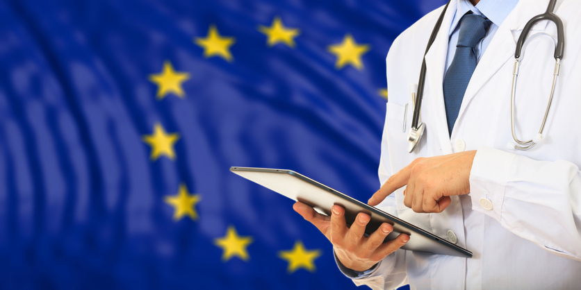 EU doctor examining mobile tablet with EU flag behind him